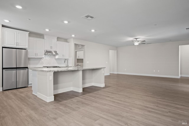 kitchen with a ceiling fan, light wood-style flooring, under cabinet range hood, visible vents, and freestanding refrigerator