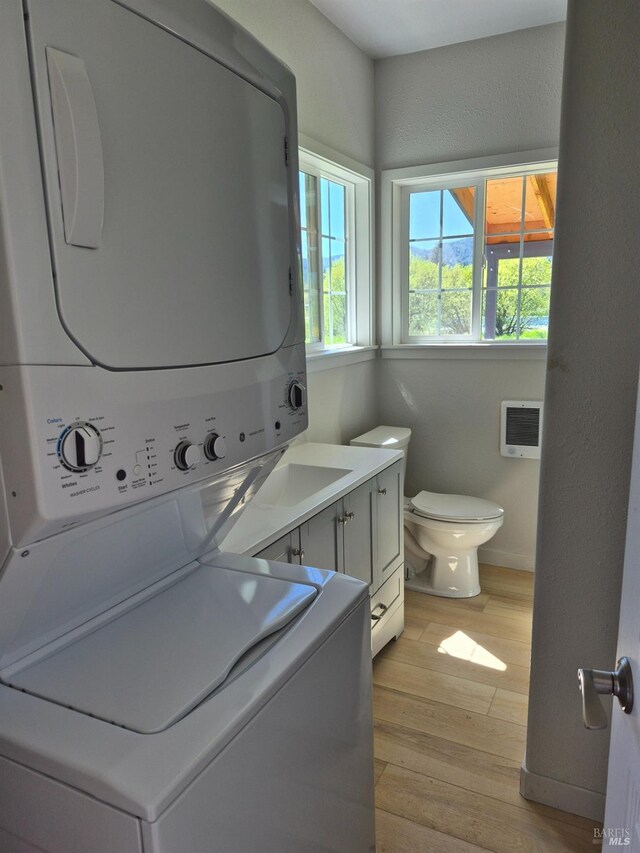 laundry room featuring a wall unit AC, stacked washer and clothes dryer, laundry area, and light wood-style flooring