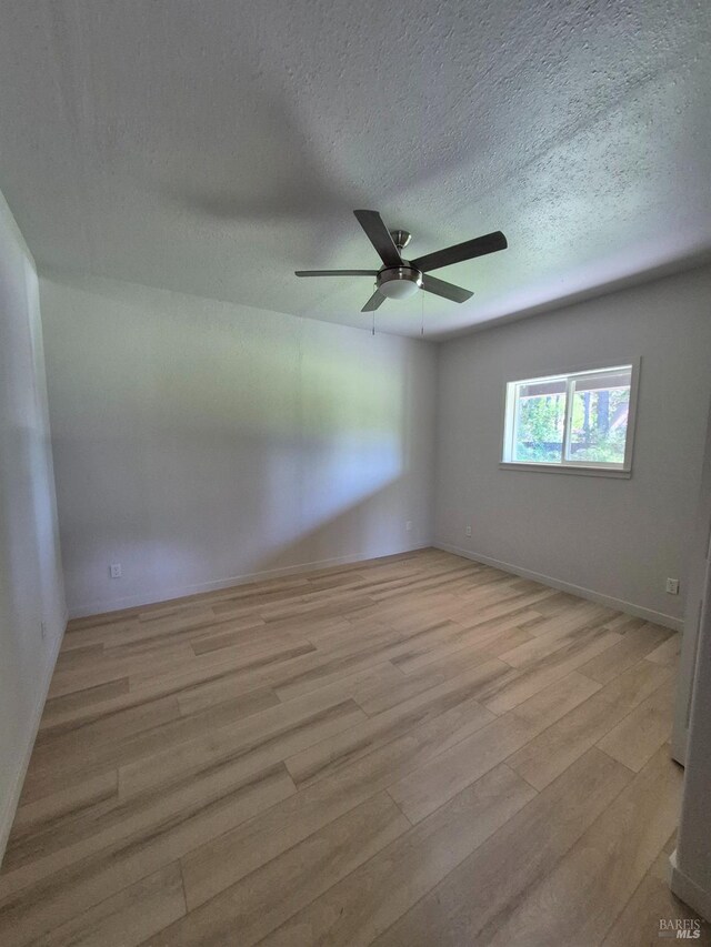 empty room with ceiling fan, baseboards, a textured ceiling, and light wood finished floors