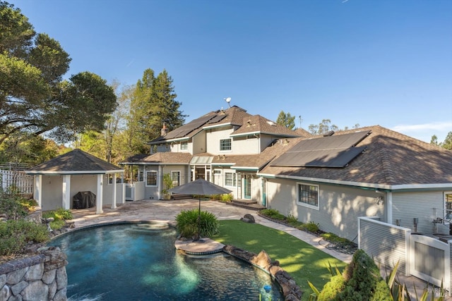 rear view of property featuring fence, an outdoor pool, a shingled roof, solar panels, and a patio