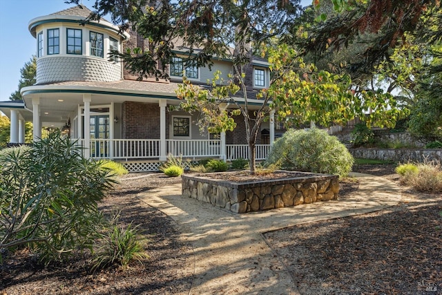 victorian-style house featuring brick siding, roof with shingles, and covered porch