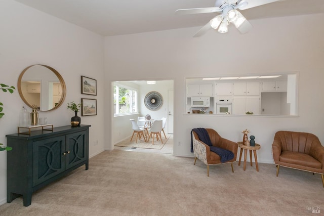 living area with ceiling fan, baseboards, and light carpet