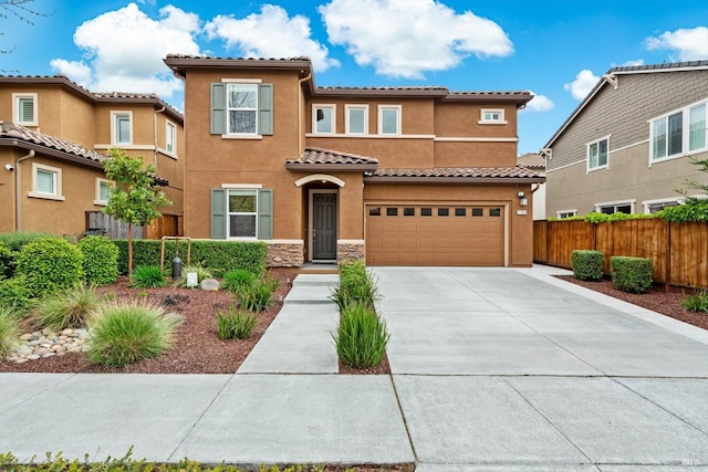 mediterranean / spanish-style home with stucco siding, fence, a tile roof, concrete driveway, and an attached garage