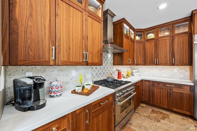 kitchen with glass insert cabinets, light countertops, wall chimney exhaust hood, stainless steel stove, and backsplash