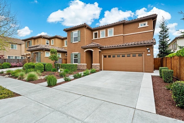 mediterranean / spanish-style house with stucco siding, fence, a tile roof, concrete driveway, and an attached garage