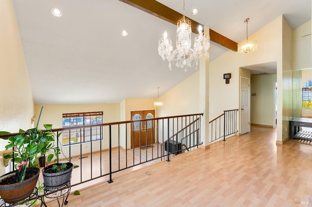 hall with an inviting chandelier, lofted ceiling with beams, wood finished floors, and an upstairs landing