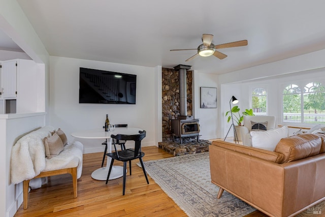 living area featuring light wood-type flooring, a wood stove, and a ceiling fan
