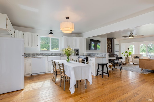 dining area featuring a wood stove, a healthy amount of sunlight, light wood finished floors, and ceiling fan