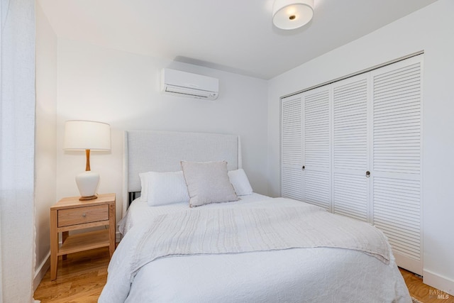 bedroom featuring baseboards, light wood-style flooring, a wall mounted AC, and a closet