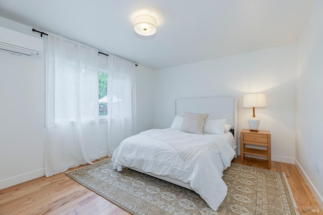 bedroom featuring light wood-type flooring, baseboards, and a wall unit AC