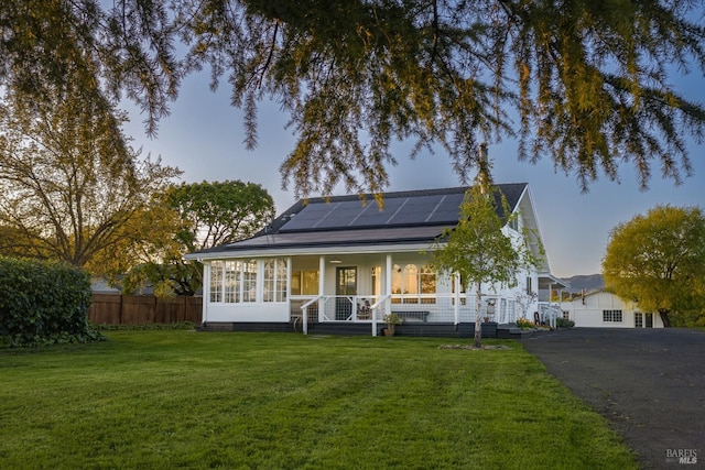 view of front facade featuring a front lawn, solar panels, driveway, covered porch, and fence