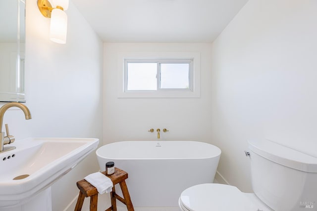 bathroom featuring a soaking tub, toilet, baseboards, and a sink