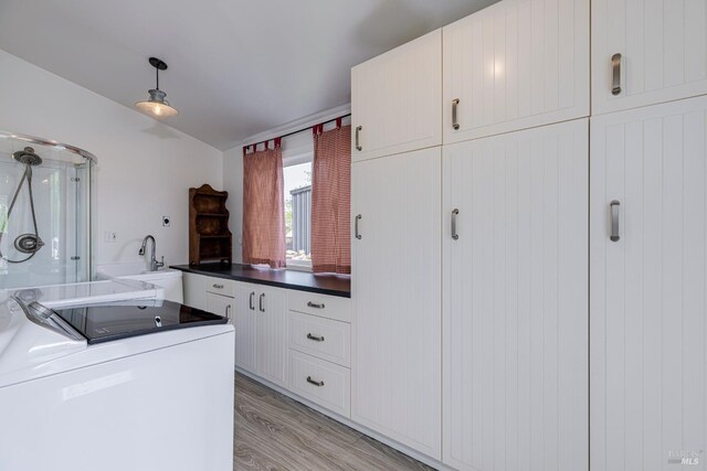 interior space featuring white cabinets, light wood finished floors, dark countertops, washing machine and dryer, and pendant lighting