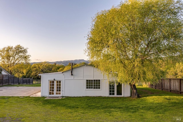 back of house at dusk with fence, a lawn, french doors, and a patio area