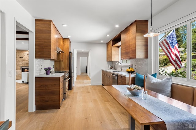 kitchen featuring modern cabinets, a sink, premium appliances, brown cabinetry, and light countertops