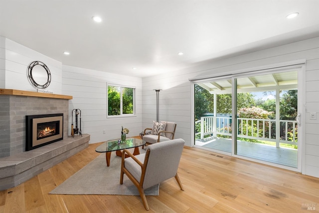 living room with recessed lighting, wood finished floors, a brick fireplace, visible vents, and wooden walls