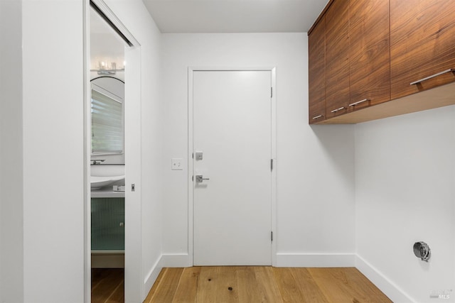 laundry room featuring light wood-type flooring, cabinet space, and baseboards