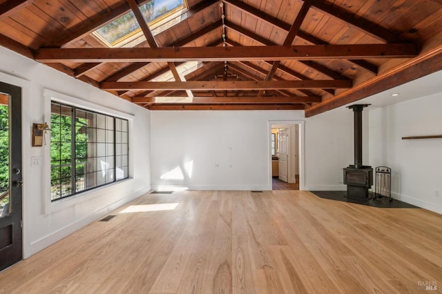 unfurnished living room featuring lofted ceiling with skylight, light wood-style floors, a wood stove, wooden ceiling, and baseboards