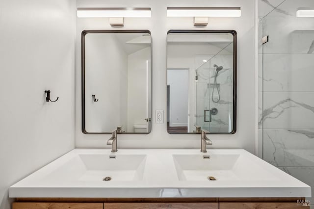 bathroom with a marble finish shower, a sink, and double vanity