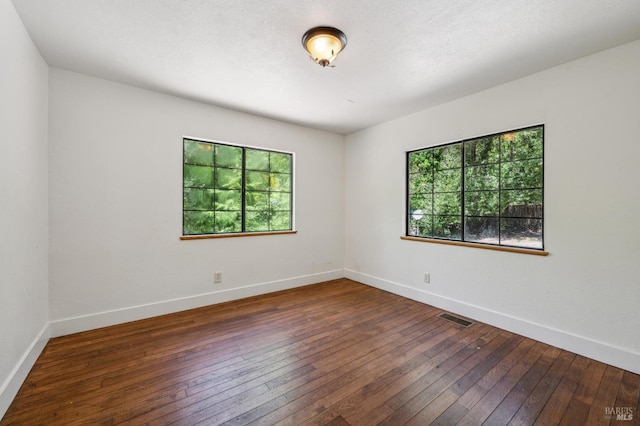 unfurnished room with visible vents, baseboards, and dark wood-type flooring