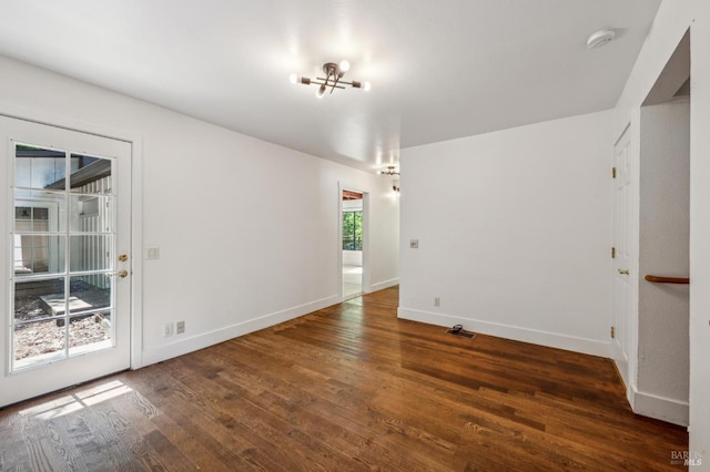 empty room featuring baseboards, wood finished floors, and an inviting chandelier