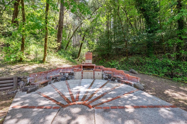 view of patio / terrace featuring an outdoor stone fireplace and a wooded view