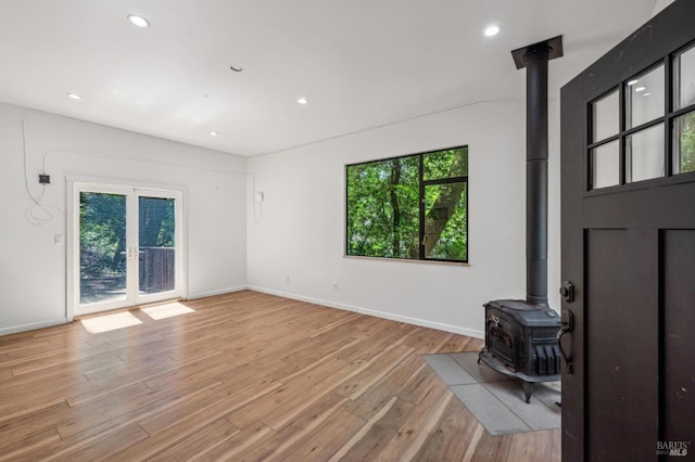 unfurnished living room with recessed lighting, a wealth of natural light, a wood stove, and light wood-style flooring