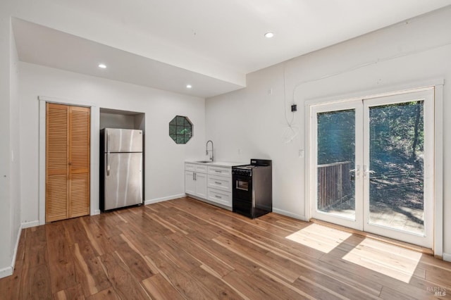 interior space with a sink, black range with electric cooktop, freestanding refrigerator, hardwood / wood-style floors, and light countertops