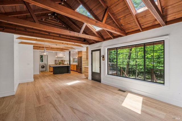 unfurnished living room with light wood finished floors, visible vents, baseboards, vaulted ceiling with skylight, and washer / clothes dryer