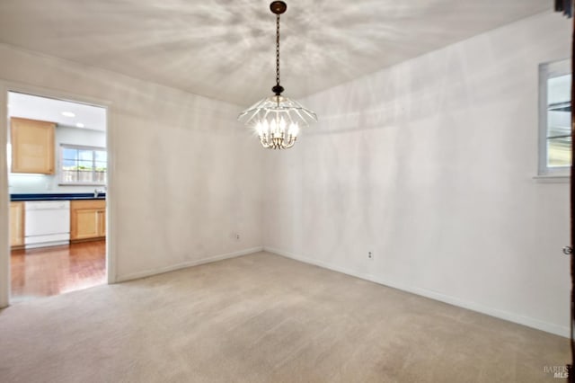spare room with an inviting chandelier, light colored carpet, and baseboards