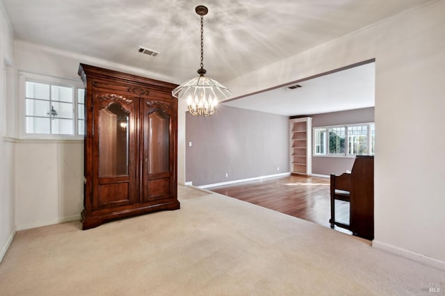 carpeted spare room with a notable chandelier, visible vents, and baseboards
