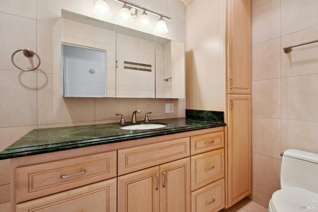 bathroom with toilet, tile walls, and vanity