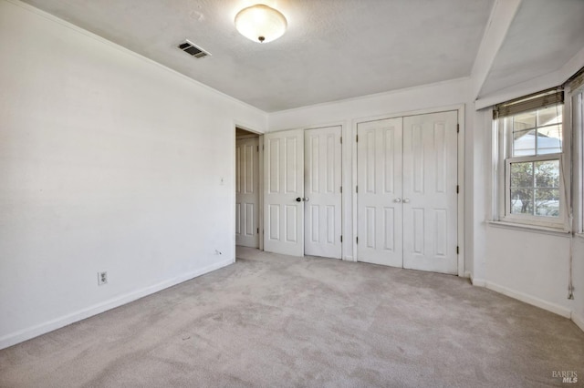 unfurnished bedroom featuring carpet flooring, visible vents, two closets, and baseboards