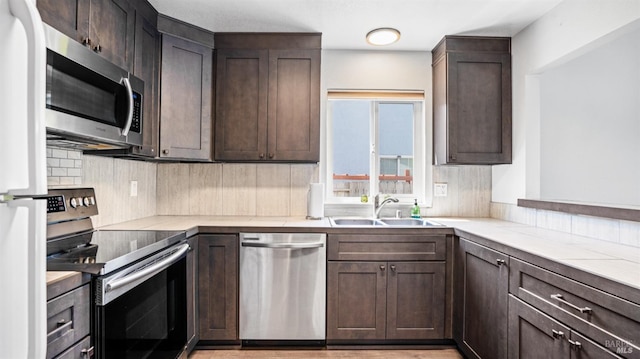 kitchen featuring stainless steel appliances, light countertops, dark brown cabinets, backsplash, and a sink