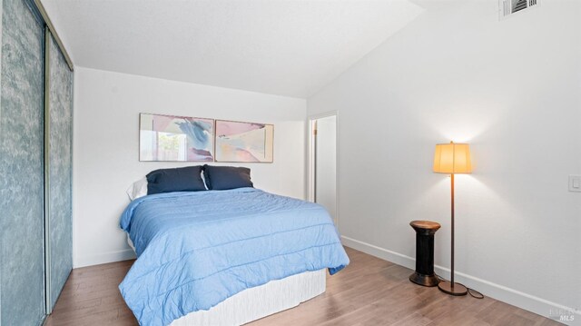 bedroom featuring vaulted ceiling, baseboards, wood finished floors, and visible vents