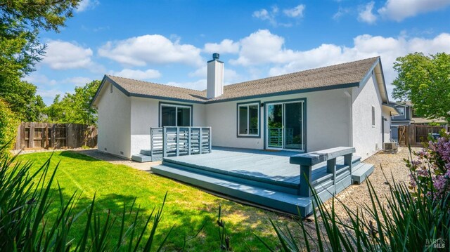 back of house with a chimney, fence, a deck, a yard, and stucco siding