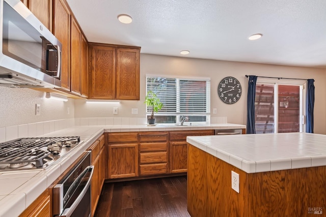 kitchen with tile counters, recessed lighting, stainless steel appliances, a sink, and dark wood-style flooring