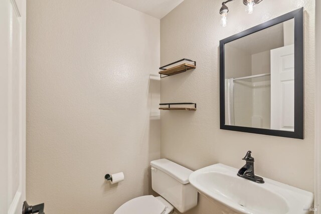 full bath with toilet, a shower with door, and a sink