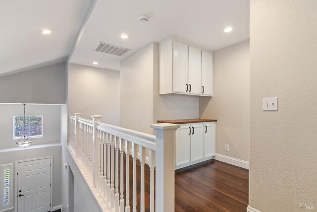 hall featuring dark wood-type flooring, visible vents, recessed lighting, and an upstairs landing