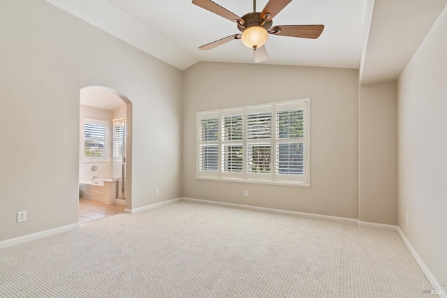 spare room featuring a ceiling fan, arched walkways, light carpet, baseboards, and lofted ceiling
