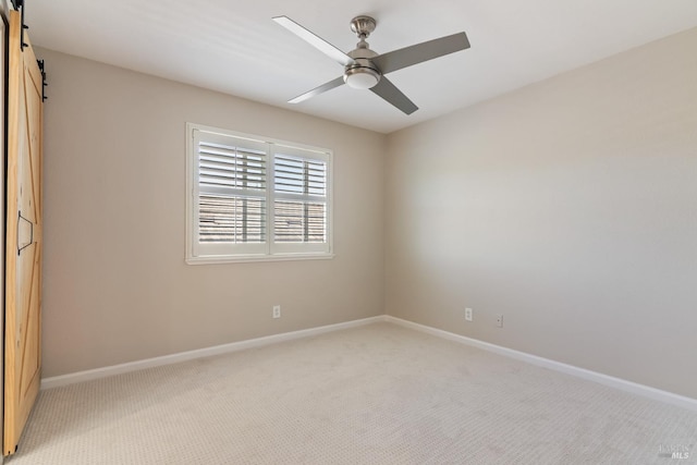 spare room with a barn door, ceiling fan, baseboards, and light carpet