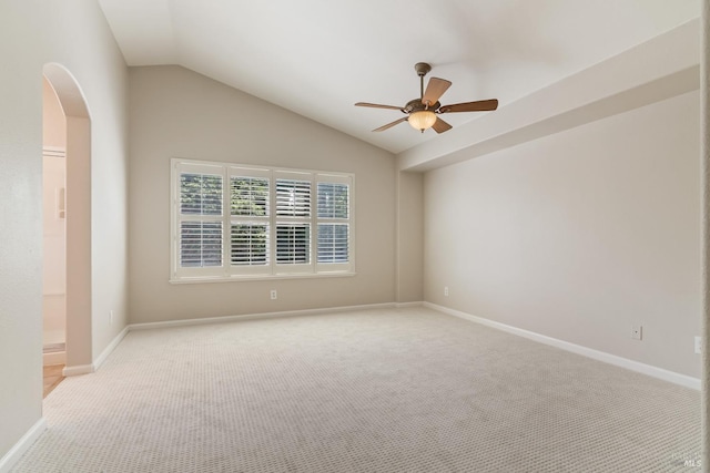 spare room with carpet flooring, ceiling fan, baseboards, arched walkways, and vaulted ceiling