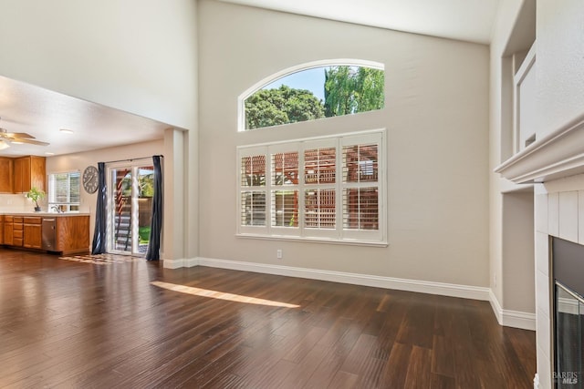 unfurnished living room featuring a towering ceiling, dark wood-style floors, a fireplace, and ceiling fan