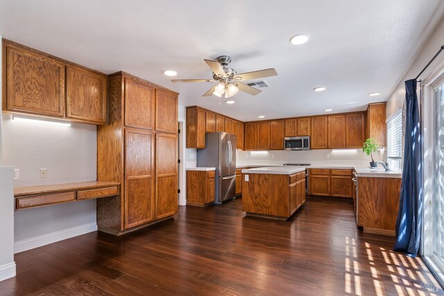 kitchen with brown cabinets, built in study area, dark wood-style flooring, and stainless steel appliances