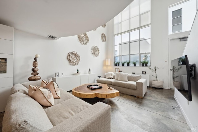 living room featuring a high ceiling, baseboards, finished concrete floors, and visible vents