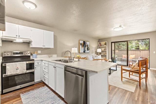 kitchen with stainless steel appliances, a peninsula, light wood-style flooring, a sink, and under cabinet range hood