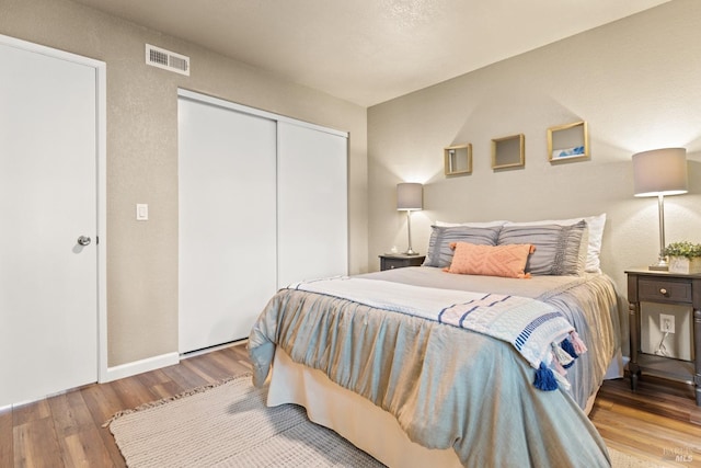 bedroom featuring a closet, wood finished floors, visible vents, and baseboards