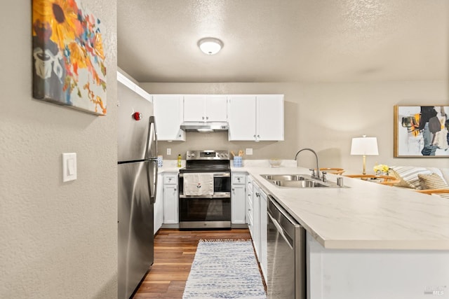 kitchen featuring dark wood finished floors, a sink, a peninsula, appliances with stainless steel finishes, and white cabinetry