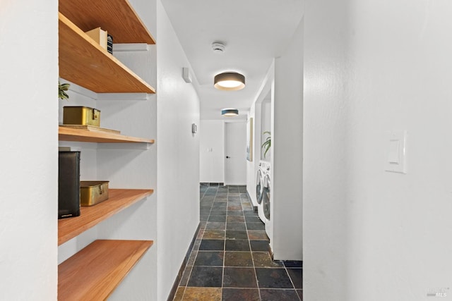 hall with arched walkways, baseboards, independent washer and dryer, and stone finish flooring