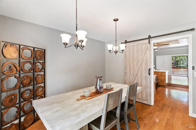 dining space with an inviting chandelier, a barn door, and light wood-style floors